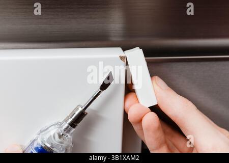 Eine Person benutzt einen Heizspachtel und einen weißen Wachsstab, um eine abgebrochene weiße Ecke zu reparieren. Möbelreparatur, Oberflächenrestaurierung Stockfoto
