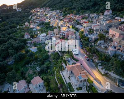 Ein Blick aus der Vogelperspektive zeigt ein Dorf am Hügel mit bezaubernder Architektur in der Abenddämmerung in der Nähe eines bewaldeten Berges. Stockfoto