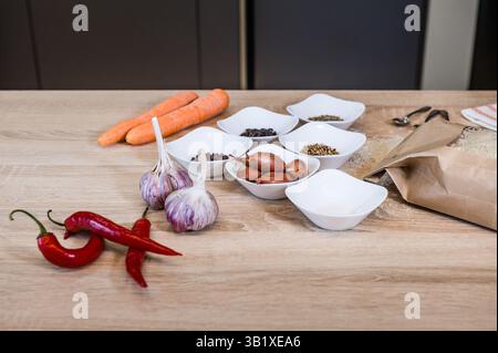 Produkte und Gewürze zum Kochen, in separaten Schüsseln auf dem Tisch. Pilaw Rezept auf Bildern. Kochschritt. Stockfoto