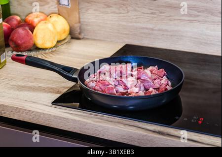 Blick von oben auf appetitliches Fleisch, das in einer Metallpfanne mit verschiedenen Gewürzen auf dem Herd während der Pilaf-Zubereitung in der Küche zubereitet wird. Stockfoto