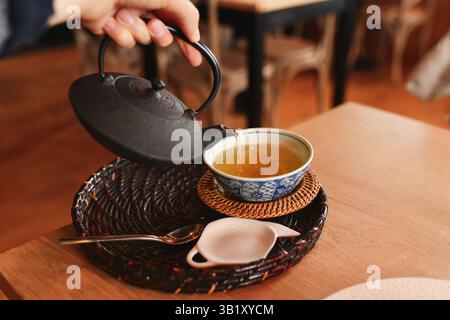 Gießt grünen Tee von Hand aus einer gusseisernen Teekanne in eine Kappe Stockfoto