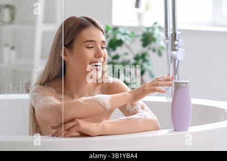 Glückliche junge Frau mit einer Flasche Duschgel, die im Bad baden geht Stockfoto