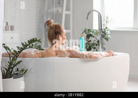 Eine hübsche junge Frau mit Schaum, die im Badezimmer baden kann Stockfoto