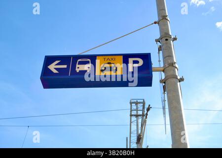 Beschilderung mit Wegbeschreibung zu Busständen, Taxidiensten und Parkmöglichkeiten, mit hellblauem Himmel und Strommasten in der städtischen Umgebung. Stockfoto