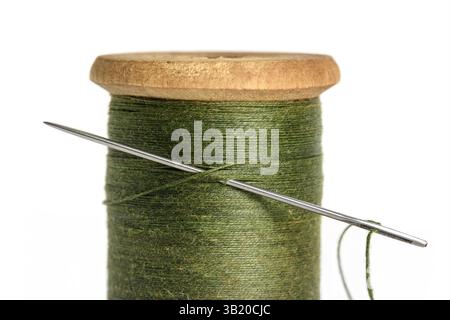 Alte einzelne Holzspule aus Garn olivgrüne Farbe und Nadel Nahaufnahme auf weißem Hintergrund Stockfoto