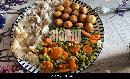 Ein Teller mit Fisch und Gemüse (Karotten, Erbsen und Kartoffelkugeln) Stockfoto