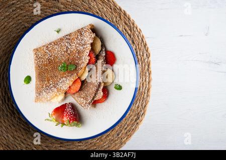 Schokoladen-Crepes gefüllt mit Erdbeere und frischer Banane. Tisch mit Blick von oben mit weihnachtsdekoration. Stockfoto