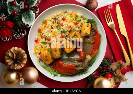 Gericht mit gebackenem Lachs, Paprika und Couscous-Salat. Tisch mit Blick von oben mit weihnachtsdekoration. Stockfoto