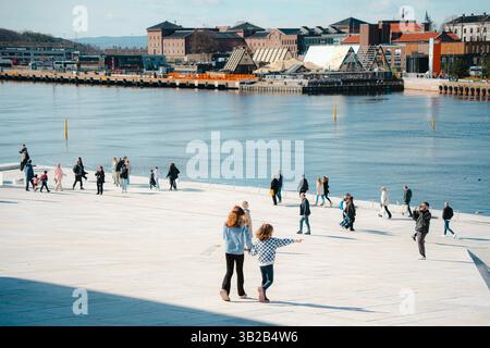 Oslo, Norwegen - 13. April 2024: Menschen, die spazieren gehen und entspannen in der Oper Oslo, Einem modernen architektonischen Gebäude mit schrägem Dach am Ufer. Stockfoto