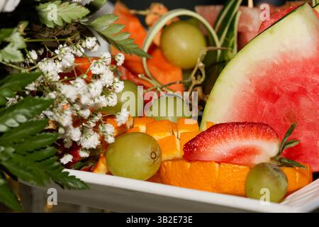 Farbenfrohe geschnittene Obstplatte auf dem Buffettisch bei einer Geburtstagsparty im Freien. Frische Sommerfrüchte für festliche Feierlichkeiten. Stockfoto