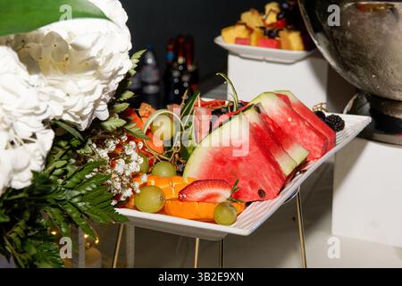 Farbenfrohe geschnittene Obstplatte auf dem Buffettisch bei einer Geburtstagsparty im Freien. Frische Sommerfrüchte für festliche Feierlichkeiten. Stockfoto