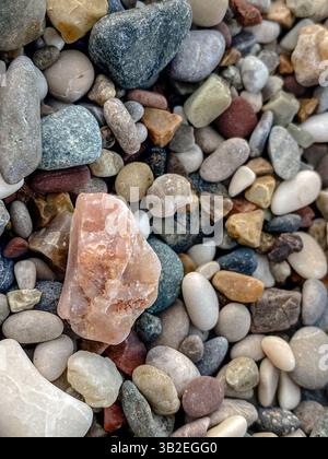 Nahaufnahme farbenfroher Kieselsteine mit einem rosa Mineralgestein in der Mitte, umgeben von glatten Steinen in verschiedenen Formen und Erdtönen Stockfoto