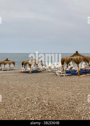 Leerer Strand mit Strohhütten und Liegestühlen an einem bewölkten Tag am Meer. Stockfoto
