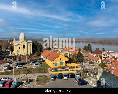 Bezaubernde Aussicht aus der Vogelperspektive auf ein farbenfrohes Dorf mit einer gelben Kirche und roten Häusern Stockfoto
