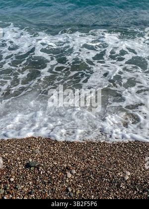 Meeresschaum und klares türkisfarbenes Wasser, das über einem Kiesstrand in Antalya, Türkei, gespült wird. Stockfoto