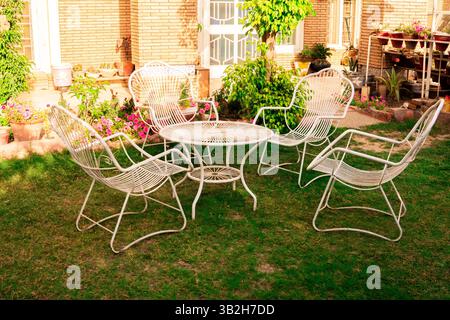 Ein ruhiger und schöner Garten mit einem weißen Tisch und Stühlen, umgeben von einer Vielzahl von bunten Blumen, ein perfekter Ort zum Entspannen Stockfoto