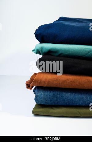 Ein ordentlicher Stapel bunter, gefalteter Hosen, die sorgfältig auf einer sauberen weißen Oberfläche platziert werden. Stockfoto