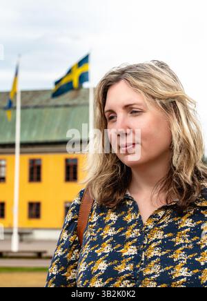 Eine Frau posiert nachdenklich mit den schwedischen und ukrainischen Fahnen, die an einem sonnigen Sommertag vor einem farbenfrohen Gebäude in Schweden steht. Stockfoto