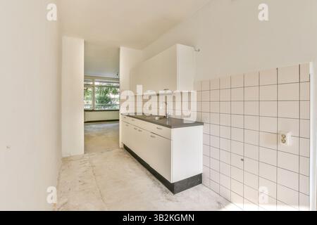 Geräumiger Küchenbereich mit eleganten Schränken, einfachen Arbeitsflächen und natürlichem Licht, das durch große Fenster strömt, schafft eine saubere und luftige Atmosphäre. Stockfoto