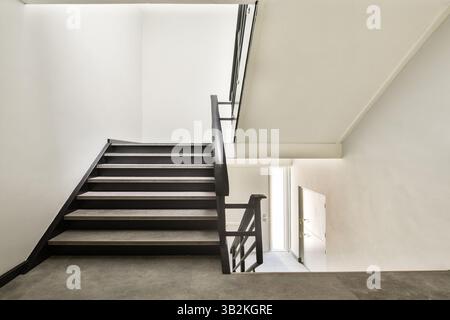 Eine saubere und einfache Treppe mit eleganten schwarzen Geländern und neutralen Wandfarben. Der lichtdurchflutete Eingangsbereich schafft ein einladendes Ambiente. Stockfoto
