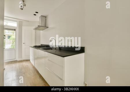 Eine elegante, moderne Küche mit weißen Schränken, schwarzen Arbeitsflächen und natürlichem Licht aus dem Fenster. Perfekte Mischung aus Funktionalität und Stil. Stockfoto