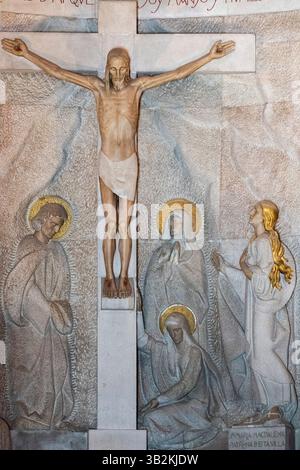 Ribadesella, Spanien - 26. April 2025: Statue des gekreuzigten Jesus Christus am Kreuz dargestellt mit Maria, Maria Magdalena und Johannes. Stockfoto