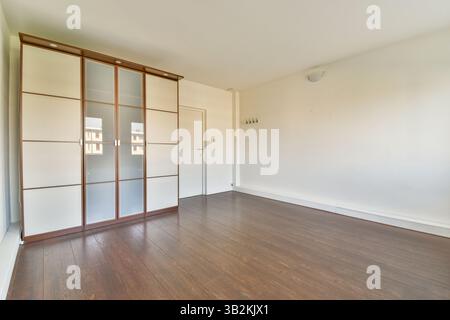Ein helles und geräumiges Zimmer mit modernem Aufbewahrungsschrank, eleganten Designelementen und poliertem Holzfußboden, perfekt für modernes Wohnen. Stockfoto