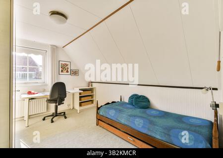 Ein schön eingerichtetes Schlafzimmer im Dachgeschoss mit einem einfachen Bett, Schreibtisch und moderner Einrichtung. Natürliches Licht filtert durch das Fenster und schafft eine einladende Atmosphäre. Stockfoto