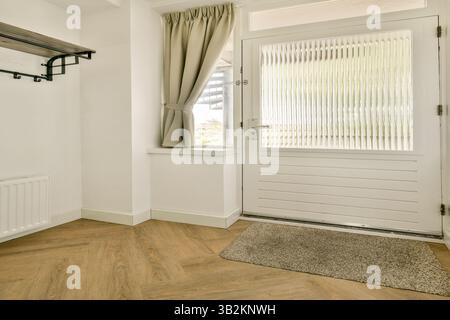 Ein moderner Eingangsbereich mit Hartholzboden, hellen Wänden und einer hellen Tür, die natürliches Licht in den Raum einlädt. Stockfoto