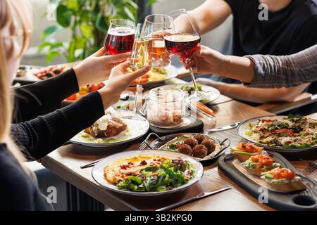 Gruppe von Freunden, die Weingläser über einem Tisch mit Gourmetgerichten anstoßen und gemeinsam in einem gemütlichen Restaurant feiern. Stockfoto