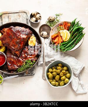 Leckere gebratene Rippchen mit gebackenen Kartoffeln, Gemüse und Oliven auf weißem Hintergrund. Draufsicht. Stockfoto