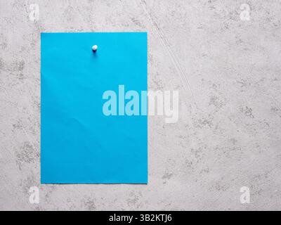 Blaues Blatt Papier, das an einer weißen Betonwand befestigt ist. Stockfoto