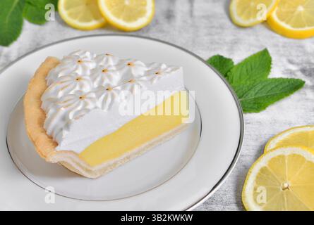 Scheibe Zitronenmeringue Pie mit Zitronenscheiben und Minzblättern Stockfoto