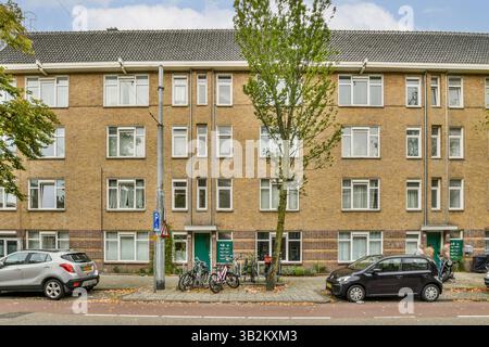 Ein modernes Wohngebäude mit mehreren Fenstern und einer Mischung aus Grün und geparkten Fahrrädern in städtischer Umgebung. Stockfoto