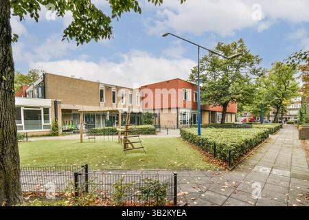 Ein ruhiger Blick auf ein modernes Wohngebiet mit einem Spielplatz inmitten üppiger grüner Rasen und Bäume. Die Architektur fügt sich gut in die Umgebung ein. Stockfoto
