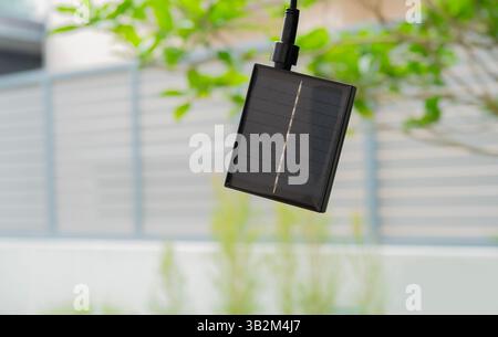 Kleine Solarbatterie-Zellenpaneel hängt am Baum im Garten zu Hause. Konzept erneuerbarer und sauberer Energie. Kopierbereich. Stockfoto