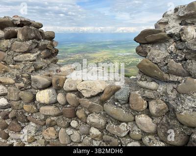 Eine alte Steinmauer mit strukturierter verwitterter Oberfläche, die sich vor der weiten offenen Landschaft des Alazani-Tals, Georgia, befindet. Ideal für Geschichte, Archit Stockfoto