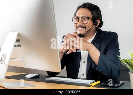 Ein junger Geschäftsmann, der Kopfhörer trägt, während er an einem Online-Meeting teilnimmt Stockfoto