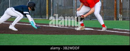 High School Baseballspieler, der während eines Pick-off-Spiels in einem Baseballspiel zur ersten Basis zurückspringt Stockfoto