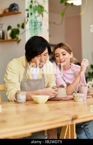 Das junge Paar bastelt gemeinsam Töpferwaren, lacht und macht Kunst in einem hellen Atelier. Stockfoto