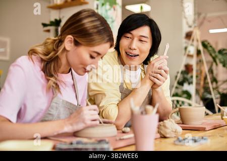 Ein junges Paar bastelt fröhlich Töpferwaren und teilt Lachen und Kreativität in einem künstlerischen Atelier. Stockfoto