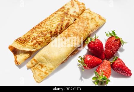 Crepes oder dünne Pfannkuchen mit Hüttenkäse und Beeren. Hausgemachte dünne Pfannkuchen, russische Blini oder französische Crepes mit Hüttenkäse und Erdbeeren. Stockfoto