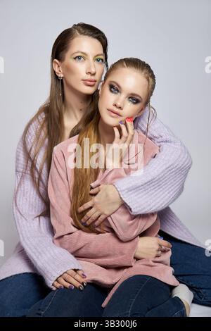 Zwei Freunde teilen einen liebevollen Moment, während sie in einem Studio posieren. Sie zeigen leuchtende Make-up-Styles vor einem neutralen Hintergrund und betonen ihre Stockfoto