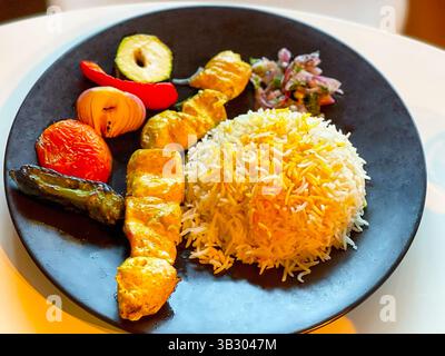 Köstlicher Hühnerkebab mit Reis und Gemüse auf einem schwarzen Teller Stockfoto