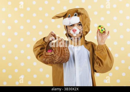 Kind verkleidet als Ostern Hase mit Korb Eiern auf gelben gestrichelten Hintergrund Stockfoto