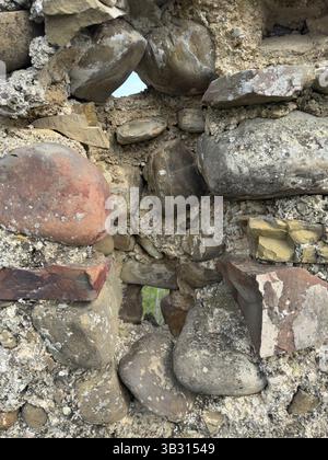 Verwitterte Steinmauer mit rauen Texturen, bedeckt mit Flecken aus Moos und Flechten, mit einer kleinen Öffnung, die hellblauen Himmel freigibt. Perfekt für sie Stockfoto