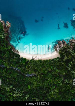 Vertikaler Blick auf den Banana Beach in Phuket, mit üppigem tropischem Dschungel, kurviger Straße und atemberaubendem türkisfarbenem Wasser. Stockfoto