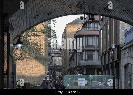 London, Großbritannien - 27. April 2025 - Fußgänger, die auf der Shad Themse spazieren gehen, sind eine historische Uferstraße neben umgebauten Waren Stockfoto