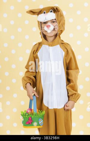 Kind verkleidet als Ostern Hase mit Korb Eiern auf gelben gestrichelten Hintergrund Stockfoto