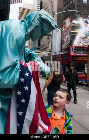 28. September 2015 - New York, New York, USA - Eine menschliche Statue in der Freiheitsstatue wird mit einem Kind in der Nähe des Times Square abgebildet. Wenn wir gute Fotos vom Times Square haben wollen, können wir in die Bar des Marriott Hotels gehen und wir werden eine tolle Aussicht haben, während wir ein Bier trinken. Fast dreißig Millionen Besucher pro Jahr durchqueren diese Gegend von ​​Manhattan, und die meisten tun dies nachts, wenn die besten Shows stattfinden. Riesige Fernsehgeräte und Hunderte von Neonschildern werben für alle Arten von Produkten und Aufführungen, und zwar zum Klang der gelben Fahrerhäuser, die sausen. So genannt, weil die Büros der New York Times hier 1904 untergebracht wurden. Es gab Stockfoto